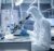 In a Secure High Level Laboratory Scientists in a Coverall Conducting a Research. Biologist Adjusts Samples in a  Petri Dish with Pincers and Examines Them Under Microscope and His Colleague Analyzes Results on a Computer.